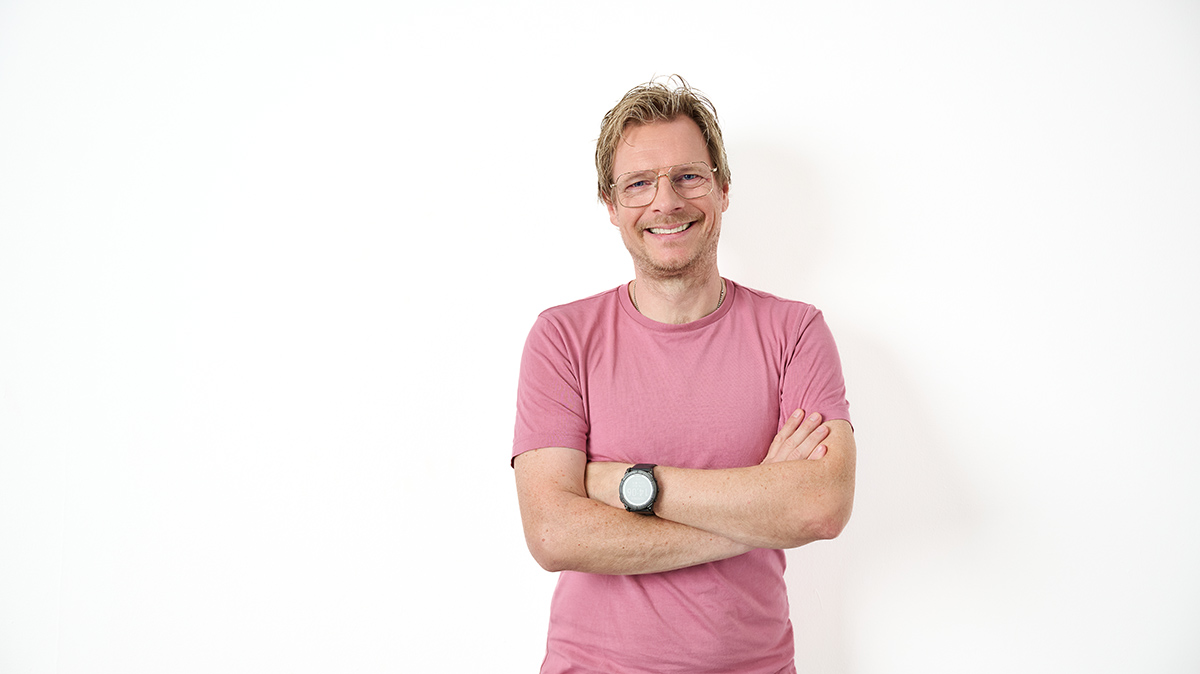 Andre Wolf lächelt in die Kamera. Er trägt ein rosa T-Shirt und eine Brille.